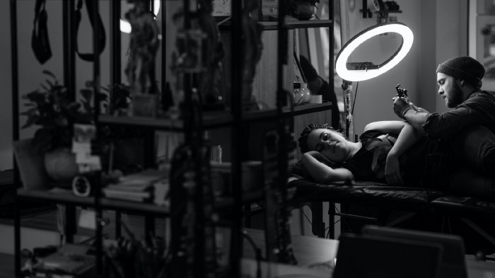 A black and white photo of a woman getting tattooed