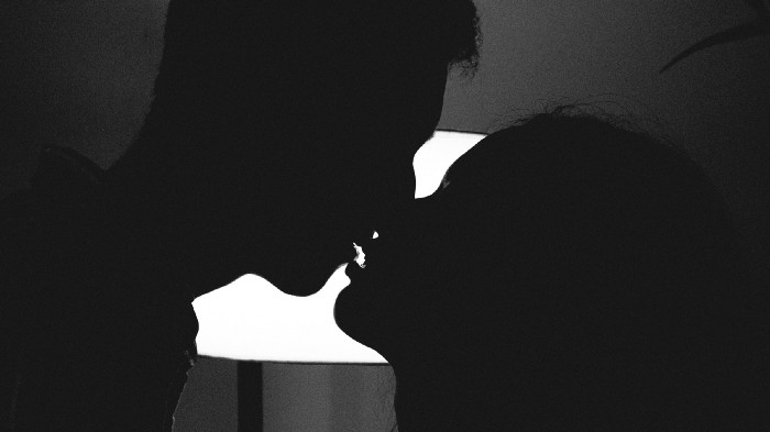 Two people in silhouette lean in for a kiss.