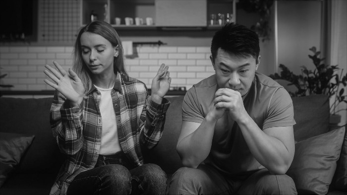 Two people sit on a couch, clearly upset with each other.